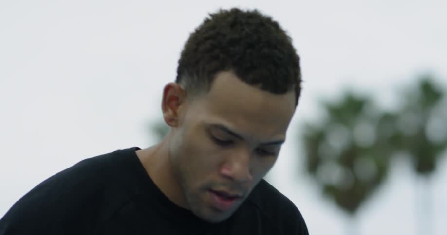 A black man looks forward intensely and then begins to dribble a basketball