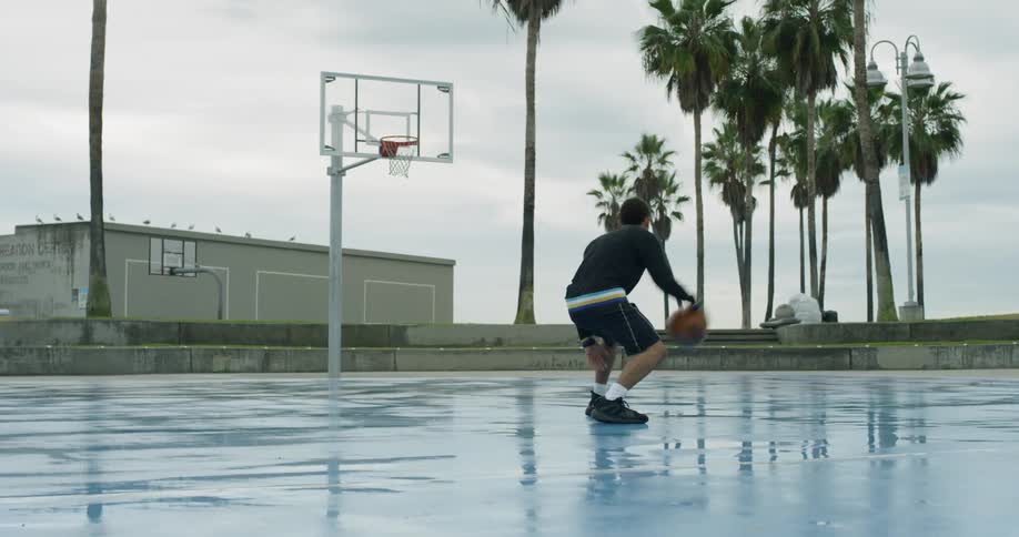 Man dribbling basketball on wet basketball court