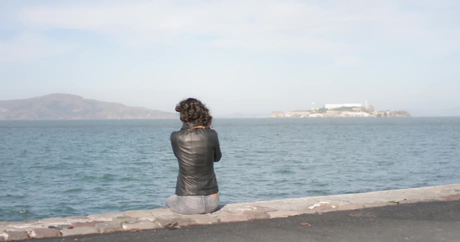 A woman sits next to the ocean