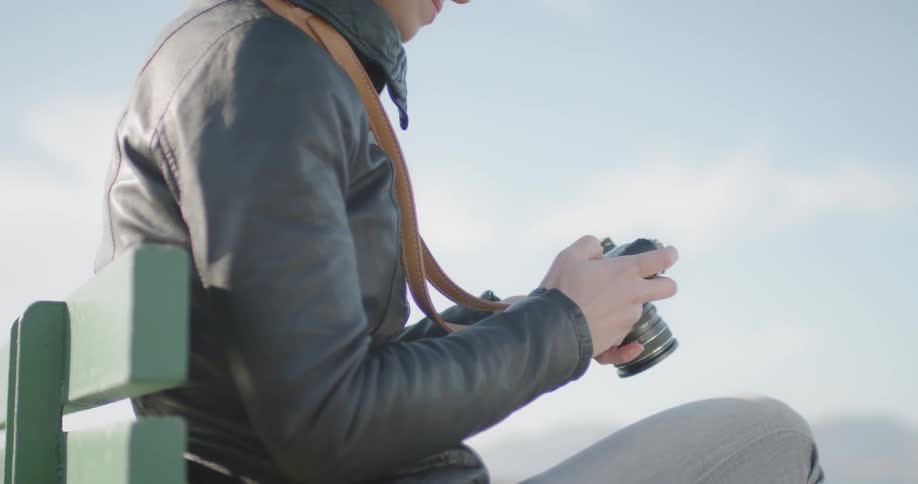 A person looks at their camera while sitting on a bench