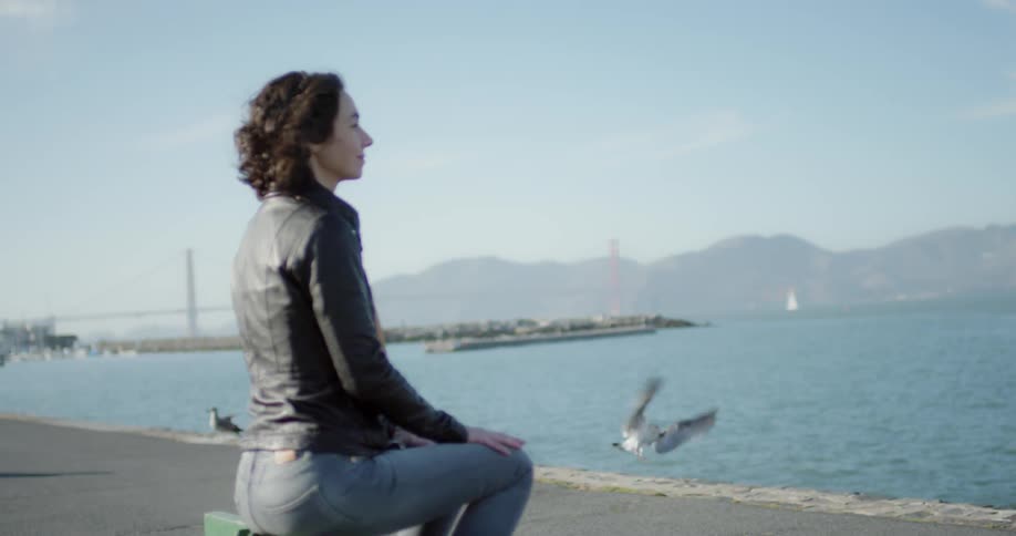 A white female sits facing a body of water with seagulls in the background
