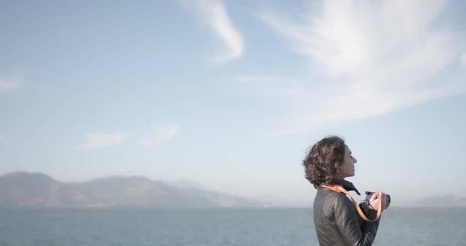 A woman with a camera looking off into the ocean