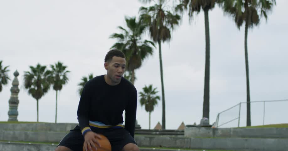 A black man dribbles a basketball back and forth under one leg before jumping up and shooting the ball
