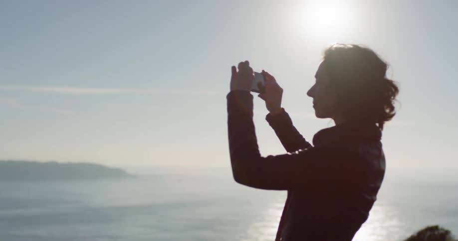 Woman takes photos of the ocean from top of hill