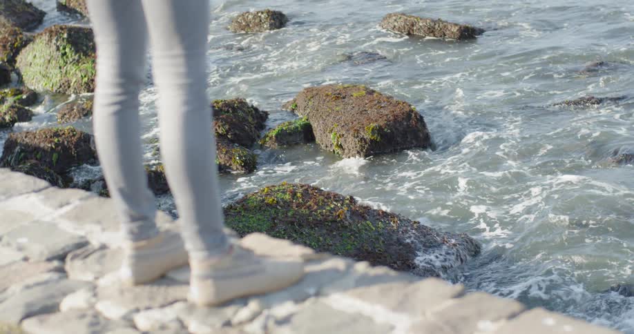 A person stands on a rock wall overlooking ocean waves