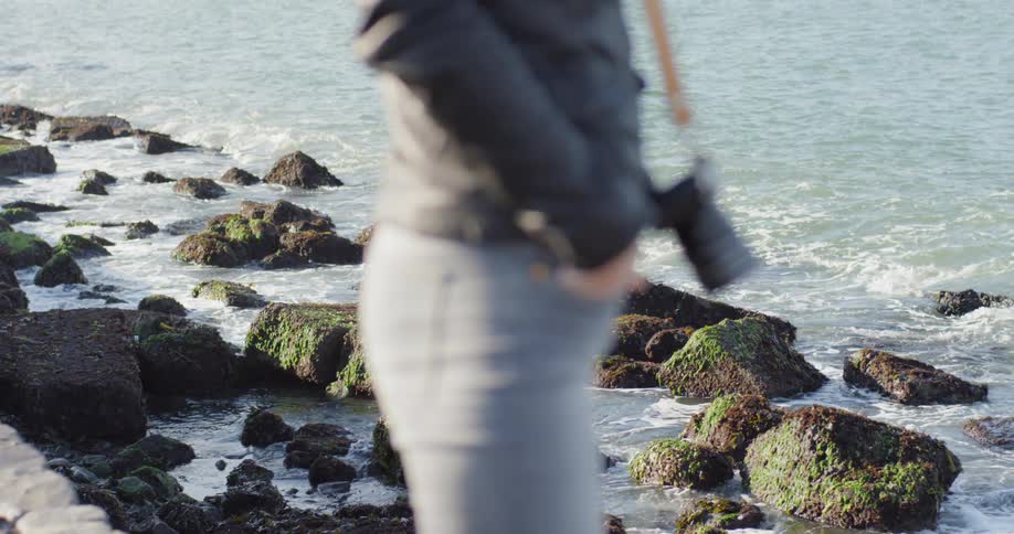 A person stands next to the ocean with a camera