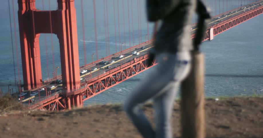 Woman stands overlooking suspension bridge holding camera