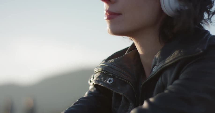 A white woman listens to headphones will sitting outdoors