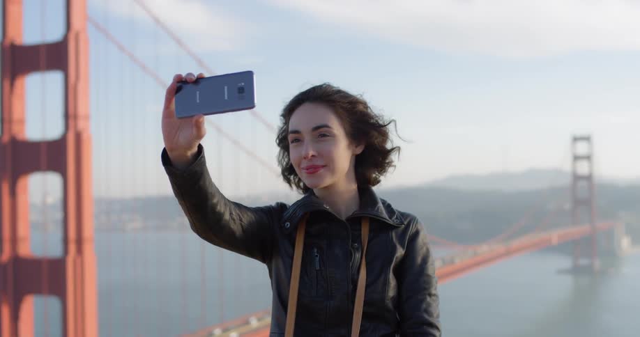 Woman takes selfie in front of suspension bridge