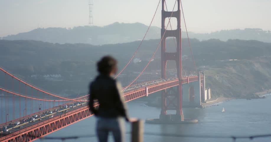 A woman is taking photographs on a hill by a bridge