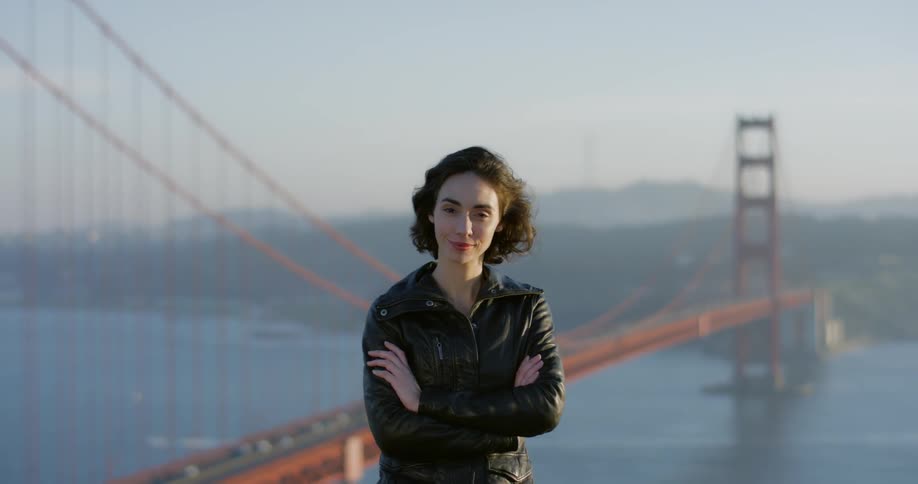 A woman is posing on a hill by a bridge