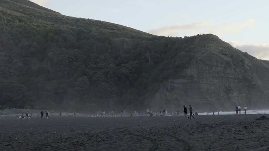 People Walking on Sandy Beach Shore Under Warm Golden Sunset Light.