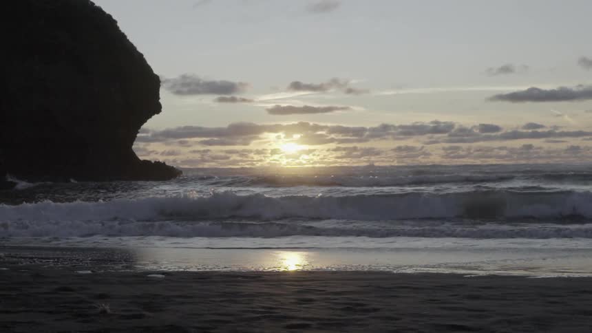Ocean Waves Washing Ashore at Sunset on Sandy Beach With Golden Light Reflection.