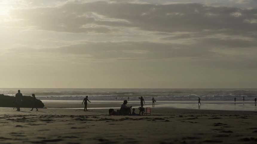 People Walking Along Beach Shoreline Under Soft Sunset Light Together.