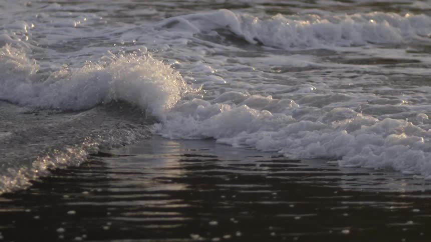 Waves are crashing on a beach on a sunny day