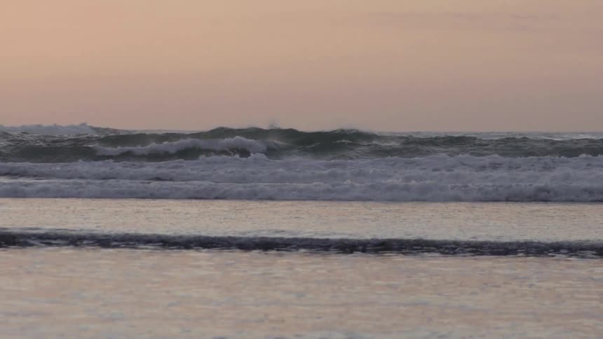 Wide shot of ocean waves rolling up onto shore,