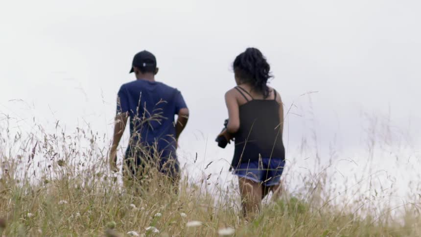 A man and woman walking up a hillside as she carries a camera