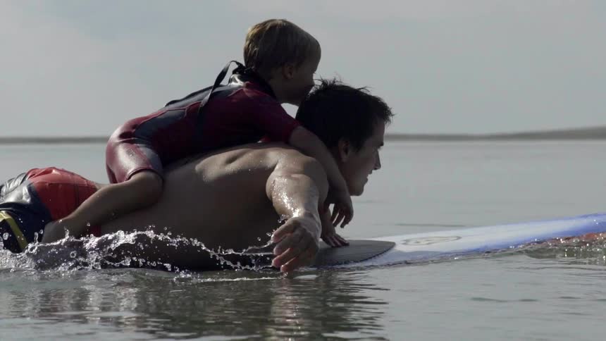 Father-Figure Surfer Paddling With Child on His Back, Sharing Trust and Joy.