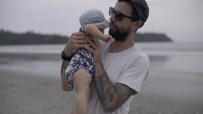 Dad Holding His Little One by the Shore, Enjoying Calm Ocean Time.