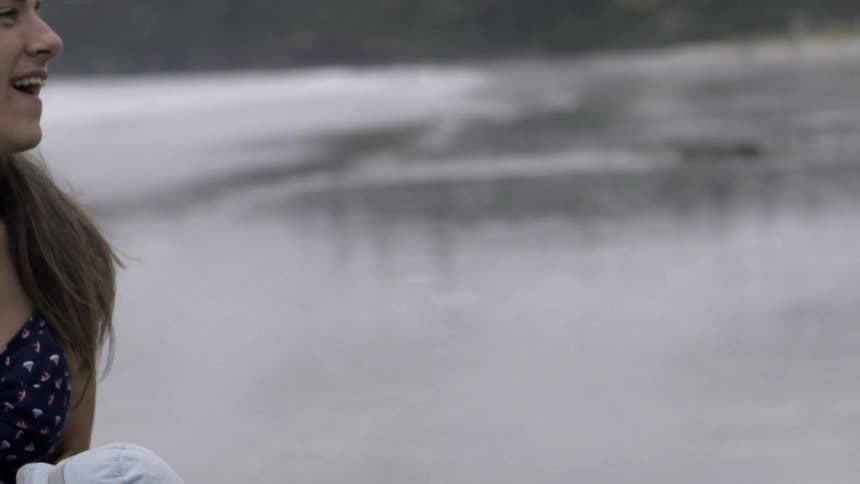 A woman swings a baby in front of a lake