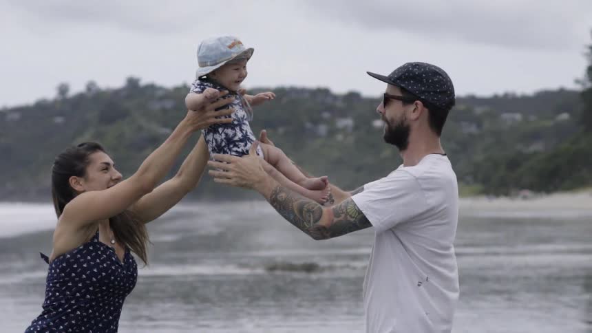 A woman tosses a baby to a man on the beach