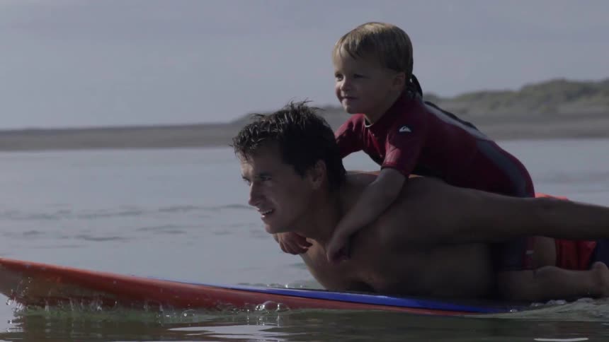 A boy is riding a mans back as he paddles on a surfboard in the water