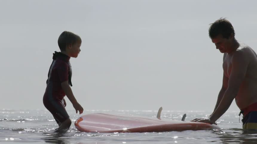 Father Guiding His Young Son as They Surf Together on Gentle Waves.