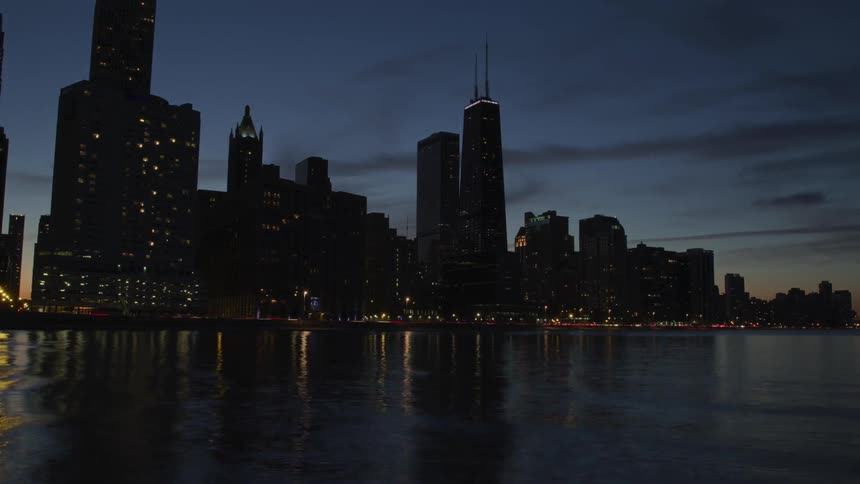 Skyline of the illuminated city while the cars go on the road next to the sea at dusk