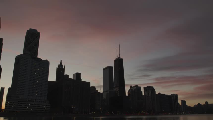 Vehicles drive along streets in front of skyscrapers after sunset