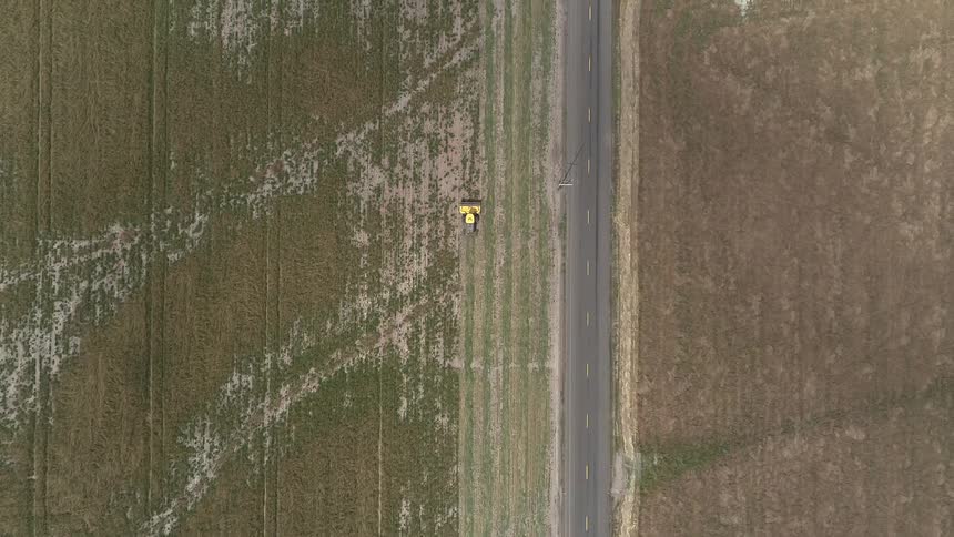 A yellow harvester modifying a field near a road during the day