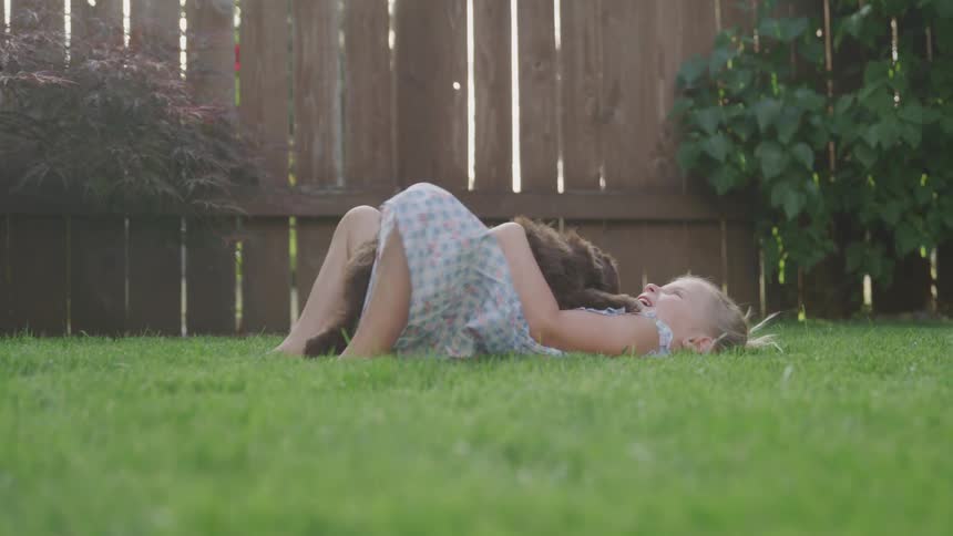 A girls lies on the grass with a puppy on her tummy