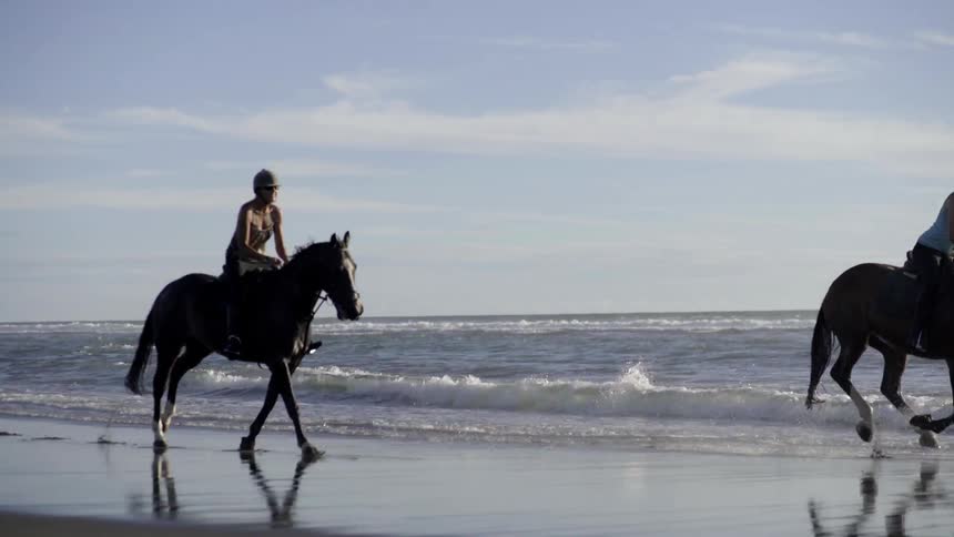People are racing horses by the shore on a cloudy day