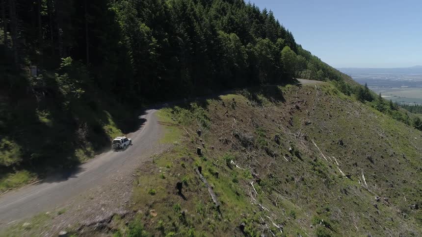 An aerial view of a white vehicle driving on a dirt mountain road