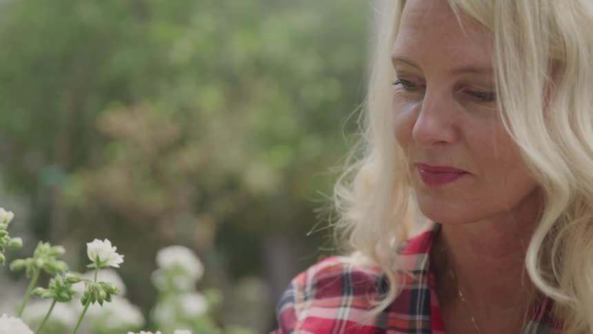 Blonde woman wearing red striped shirt looks at the flowers during daylight