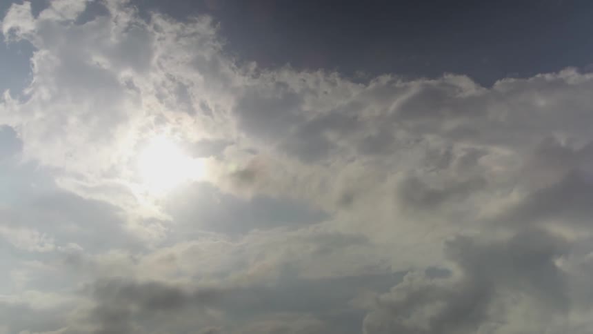Fluffy clouds are blowing swiftly across the sky as the sun peeks through and shines brightly