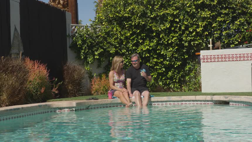 A man and woman sit on the ledge with their feet in a pool