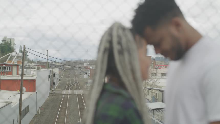 A couple touch foreheads and smile on an overpass above train tracks