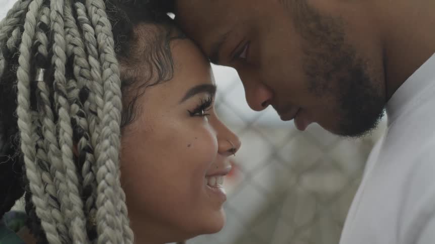 A young man and woman pressing their foreheads together before a fence