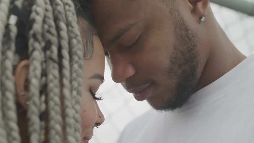 A young man and woman smile at each other as they lovingly press their foreheads together