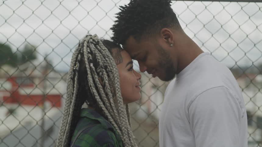 Couple stand close with foreheads pressed together near chain link fence