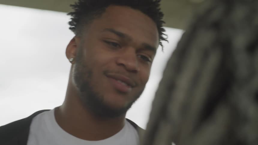 A boy standing outside talking to a girl scratches his nose and laughs
