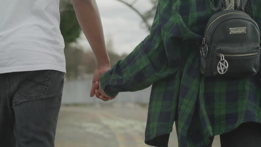 Man in white shirt and jeans and woman in green plaid shirt holding hands as they walk