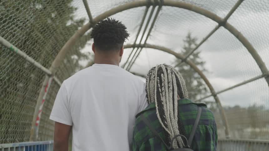 A man and woman walk through a chain link tunnel