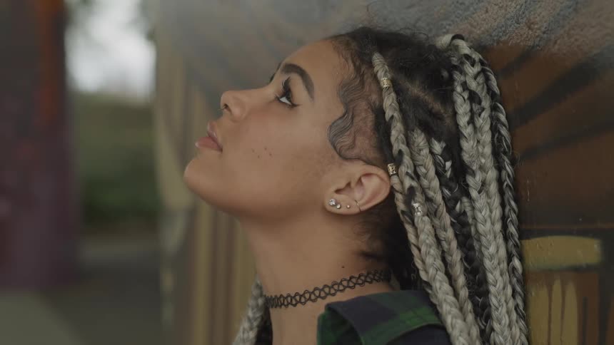 A young black woman leaning against a wall and looking upwards