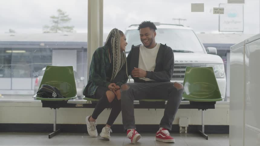 A young man and woman sitting together in the lobby of a business talking with each other playfully