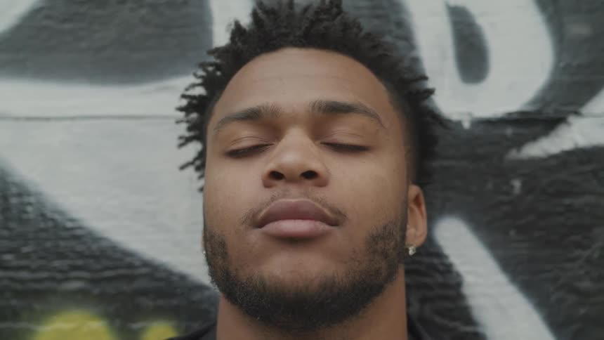 A black man leaning against a wall covered in graffiti