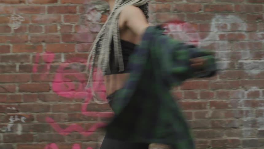A woman dances in front of a brick wall