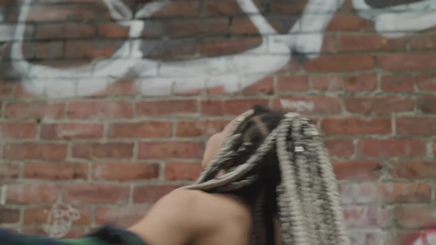 A woman spins in front of a brick wall with graffiti