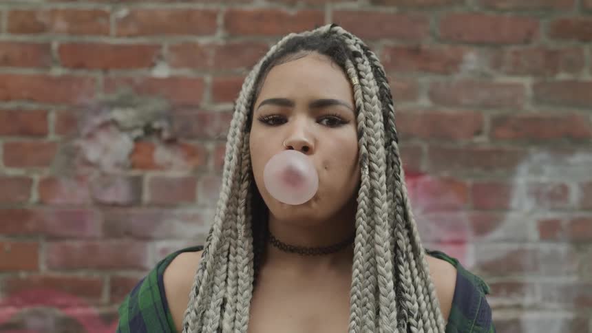 A woman blows a bubble with bubble gum