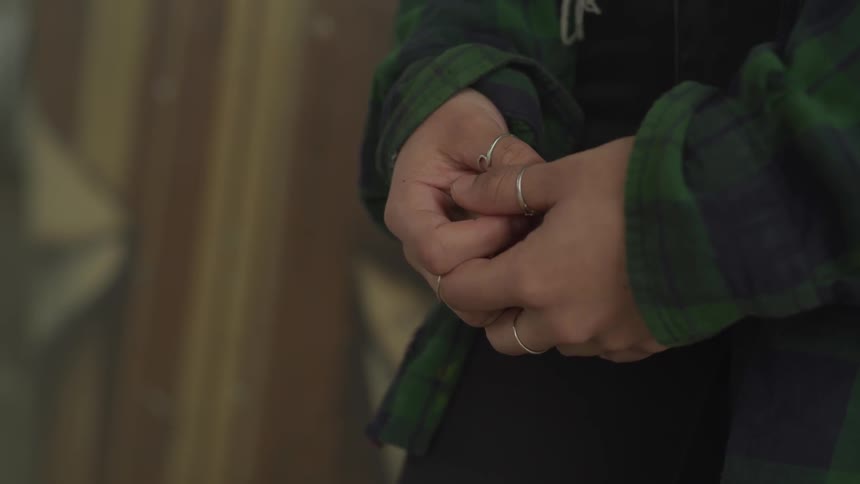 A person with rings on their fingers wearing a flannel shirt with hands clasped